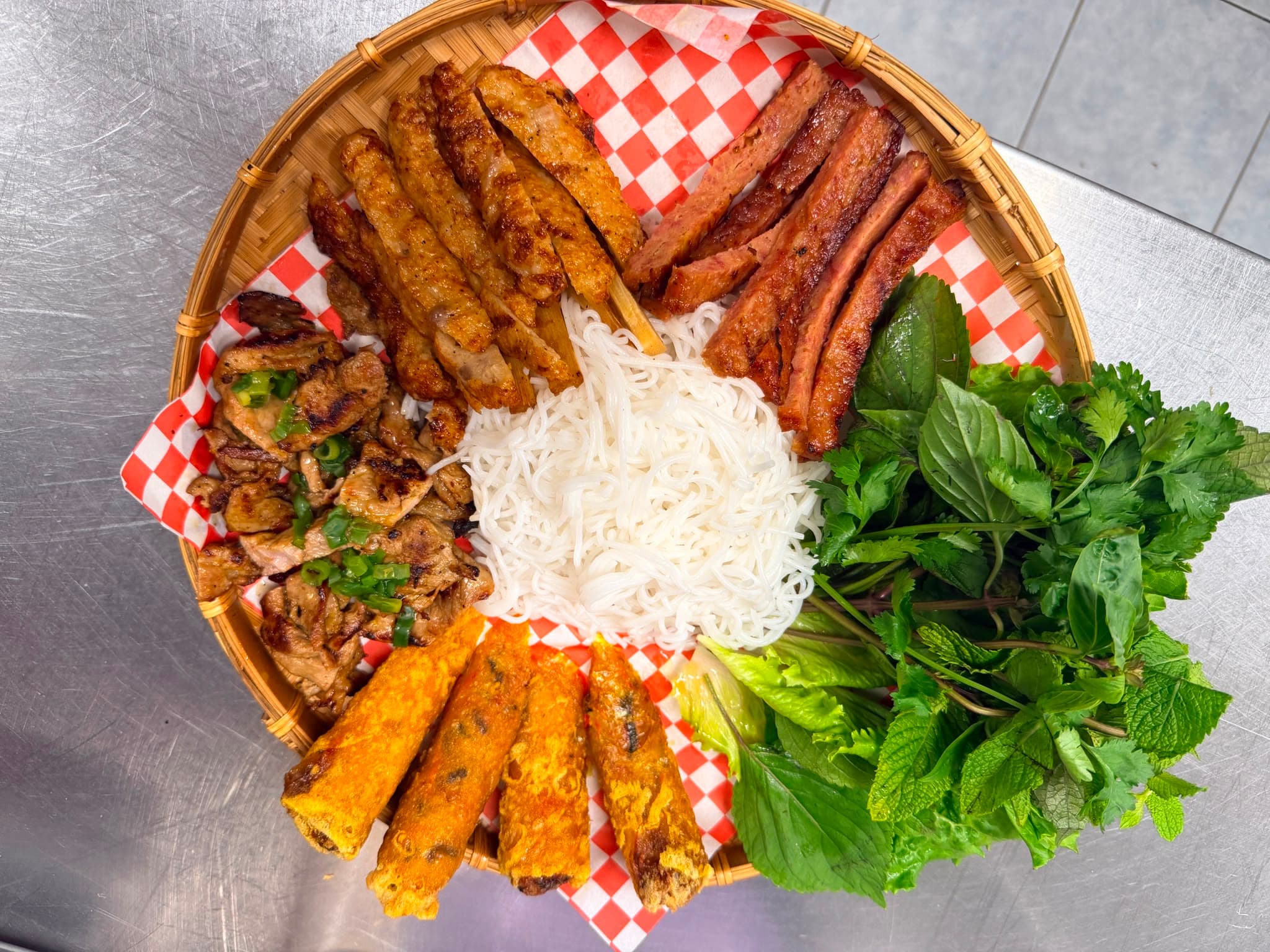 Vietnamese bamboo platter with rice vermicelli, grilled meats, fried spring rolls, and fresh herbs.